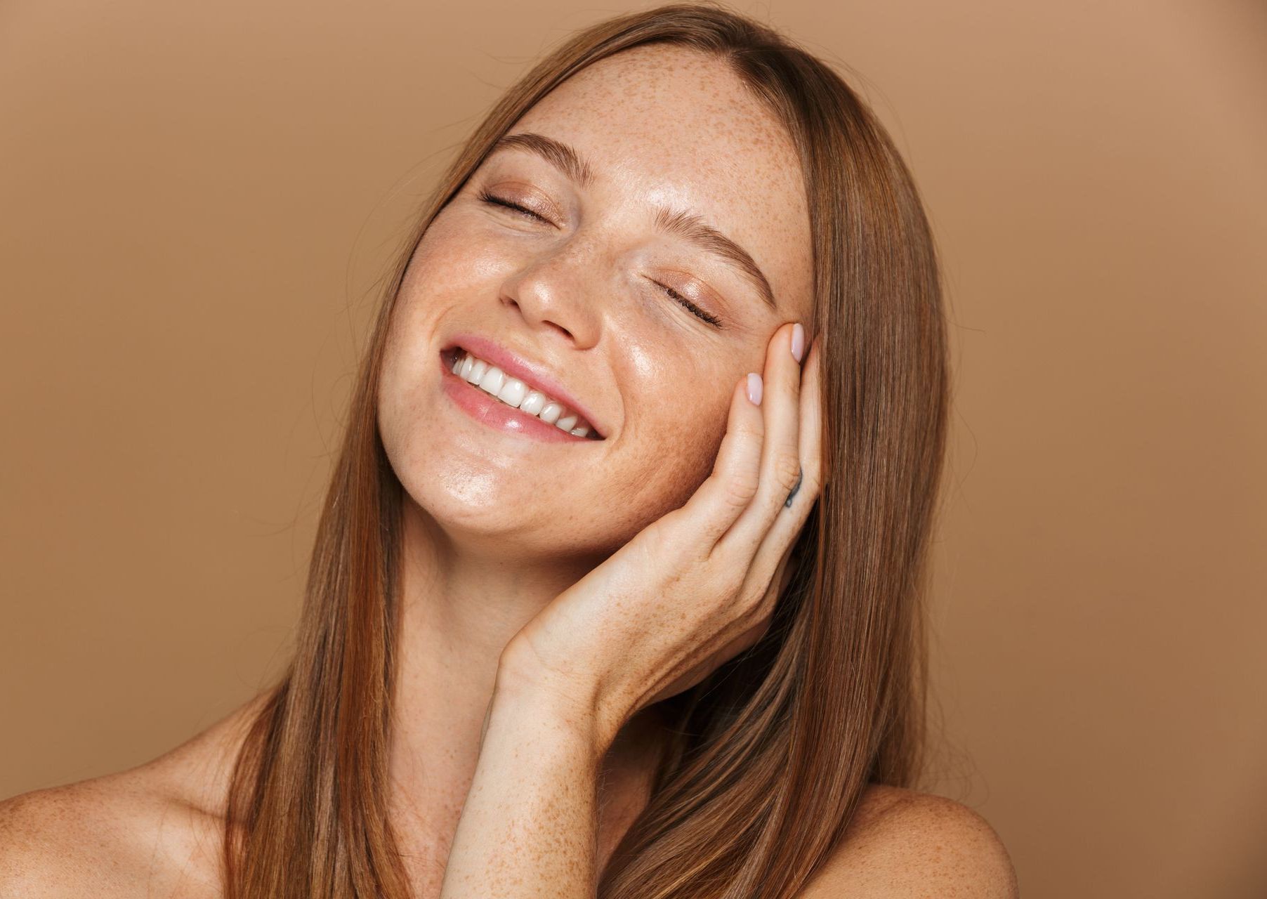 A close up portrait of a smiling woman touching her face