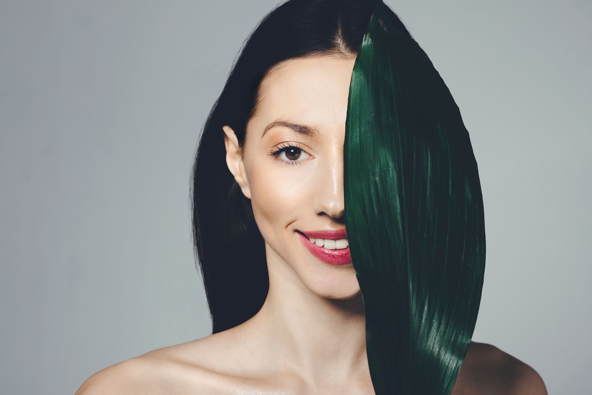 A woman with green hair is covering half of her face with a green leaf.