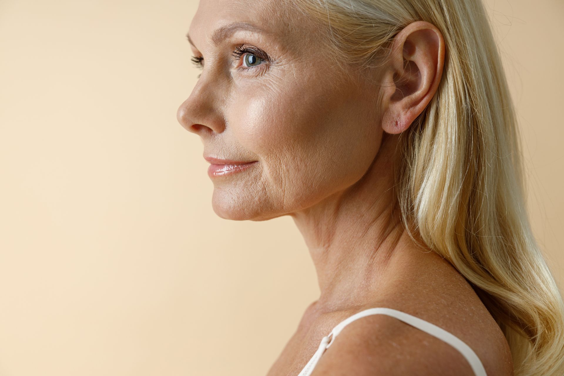A close up of an older woman 's face against a beige background.