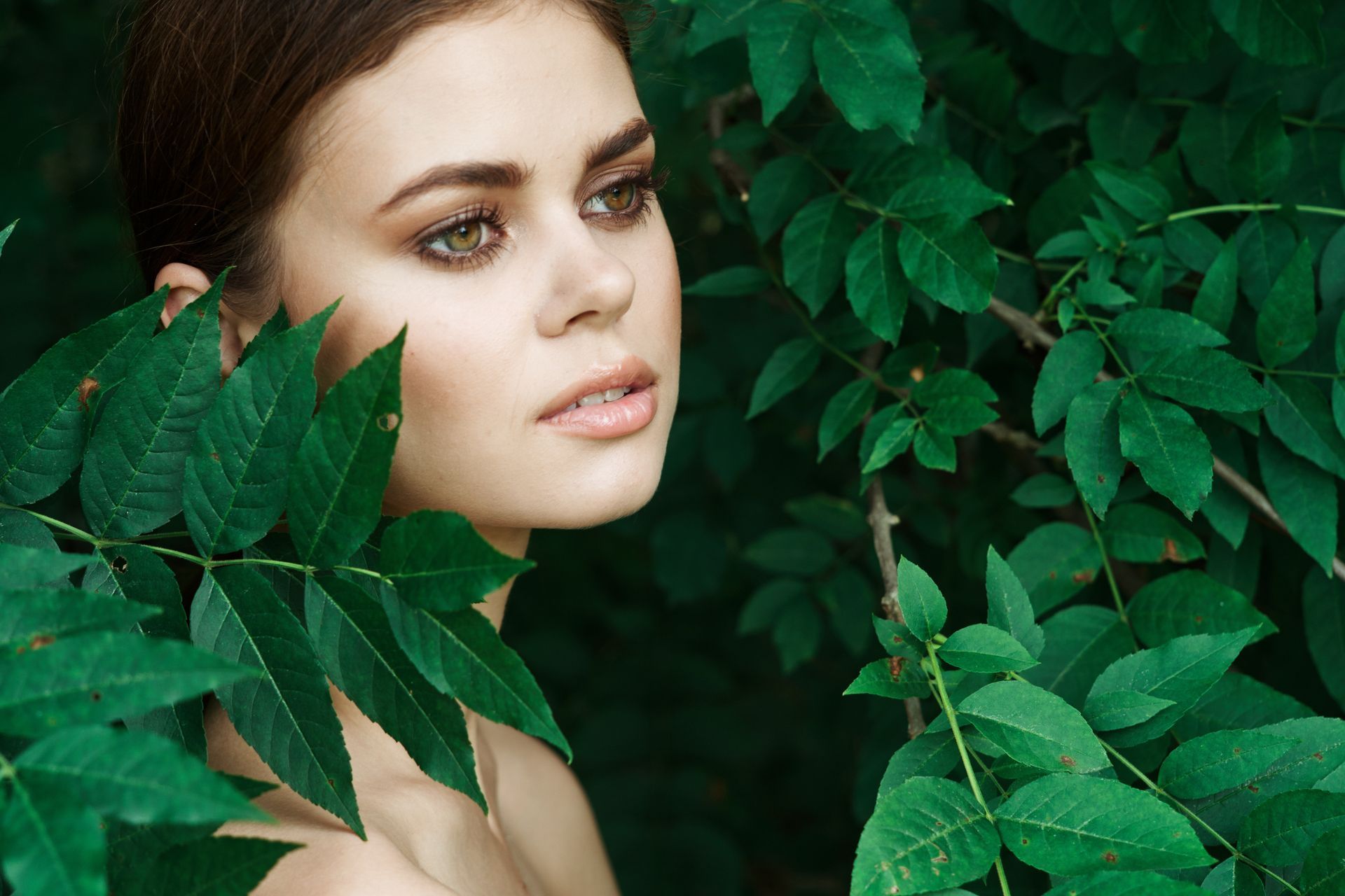 A woman is standing in a forest surrounded by green leaves.