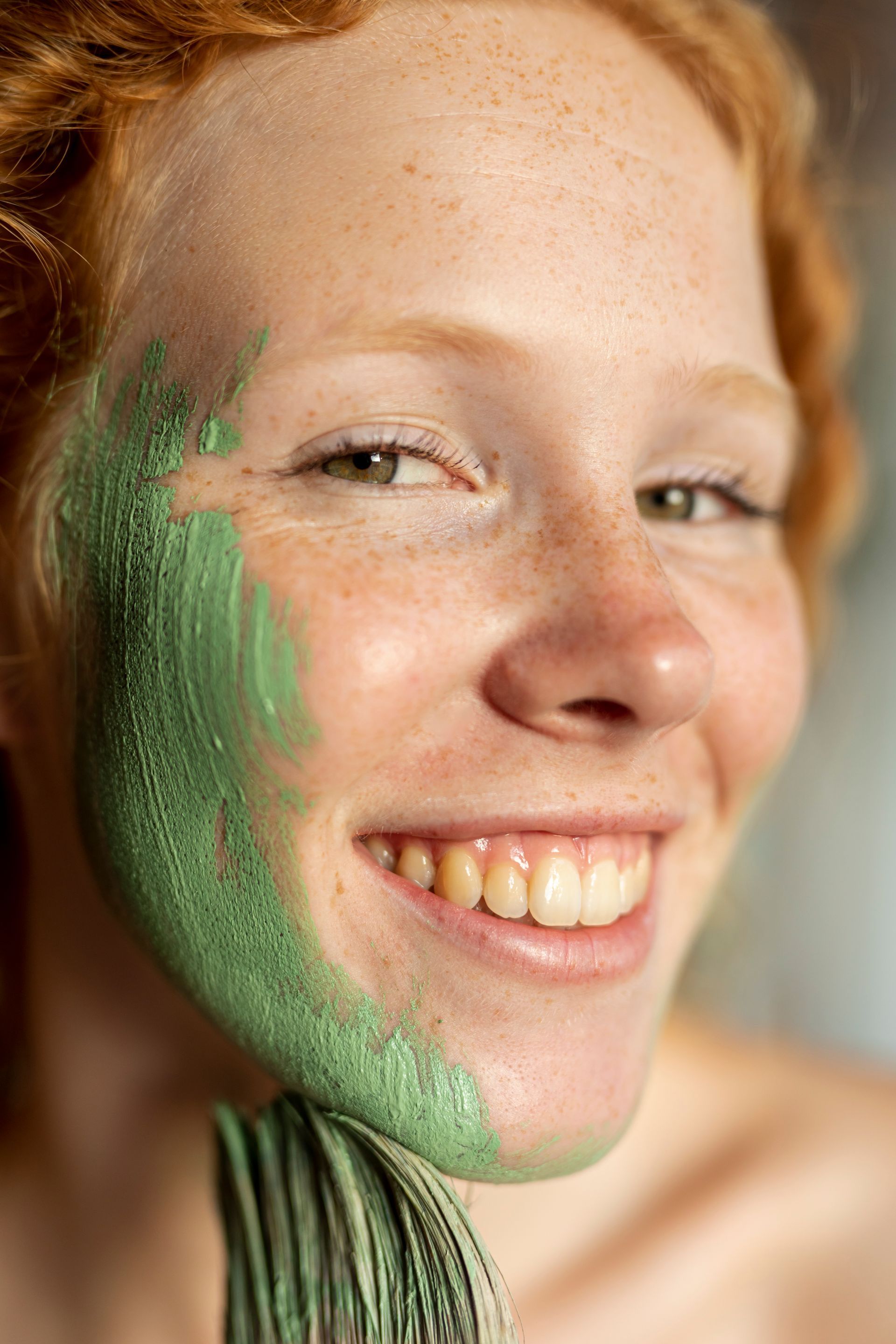 A woman with a green mask on her face is smiling.