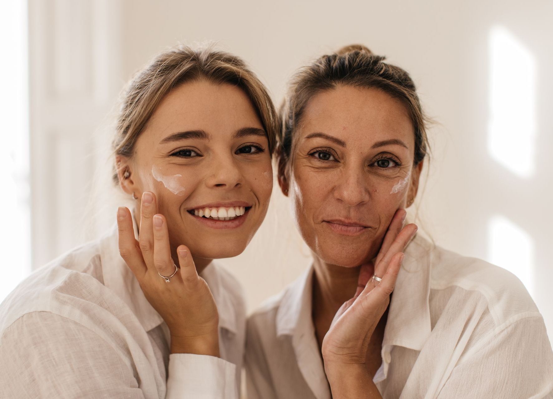 A young woman and an older woman are applying cream to their faces.