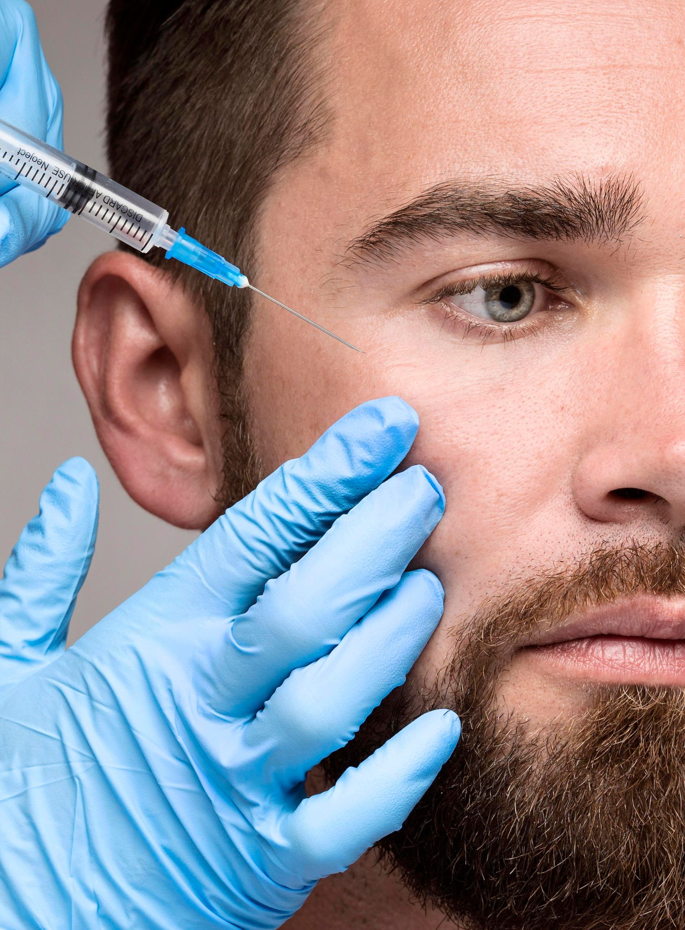 A person receiving a facial injection near the eye, blue gloves, syringe, focused expression.