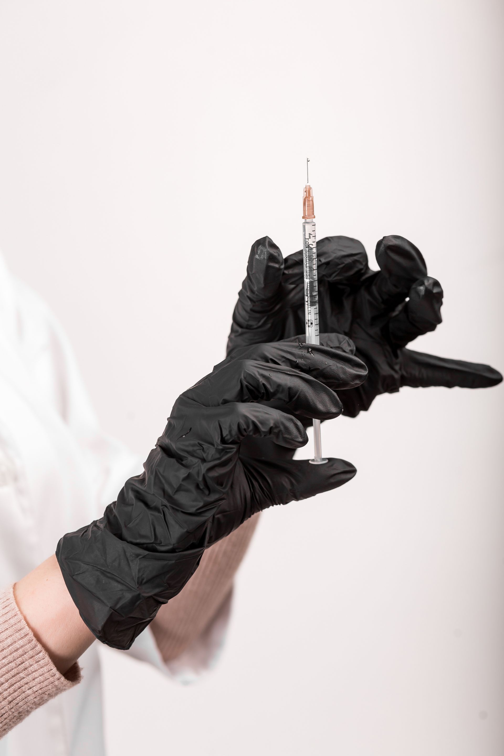 A person wearing black gloves is holding a syringe in their hand.