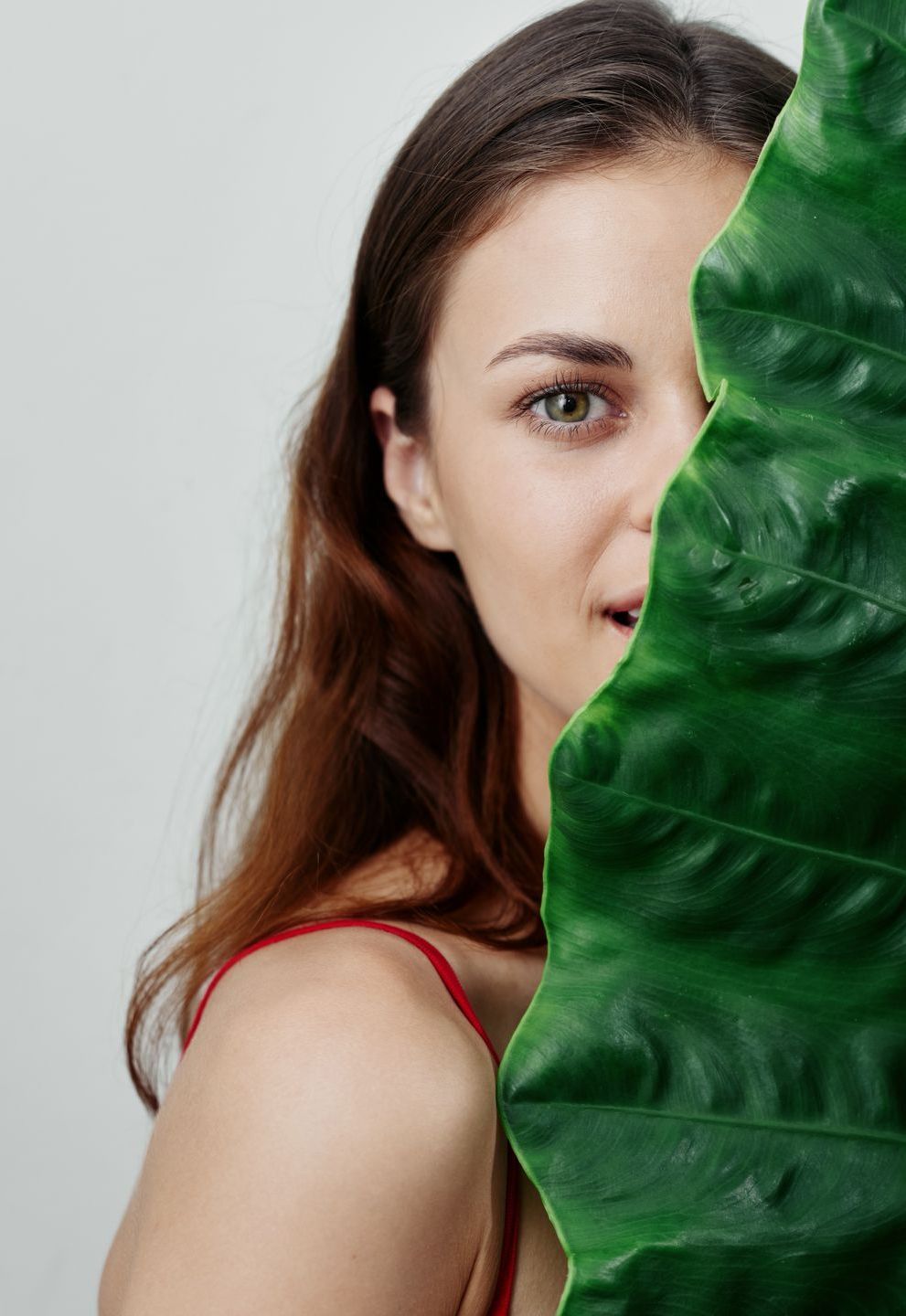 A woman is covering her face with a green leaf.