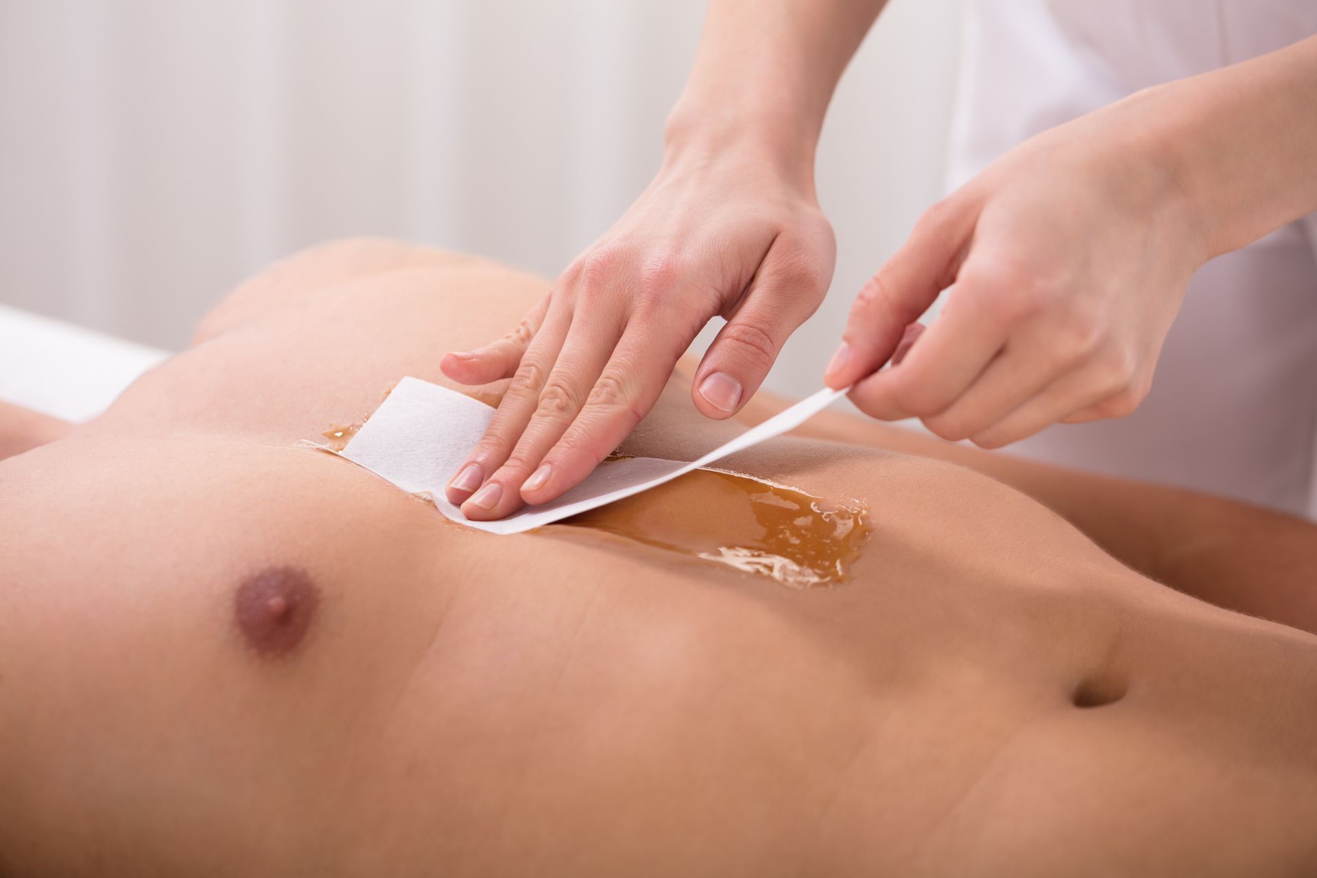 Person having chest waxed at a spa; hands pressing a wax strip on skin.
