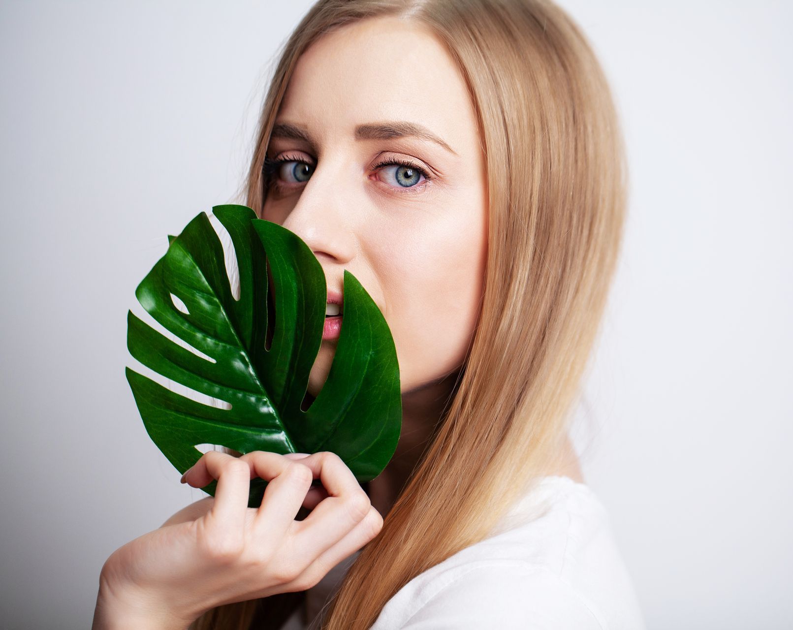 A woman is holding a green leaf in front of her face.