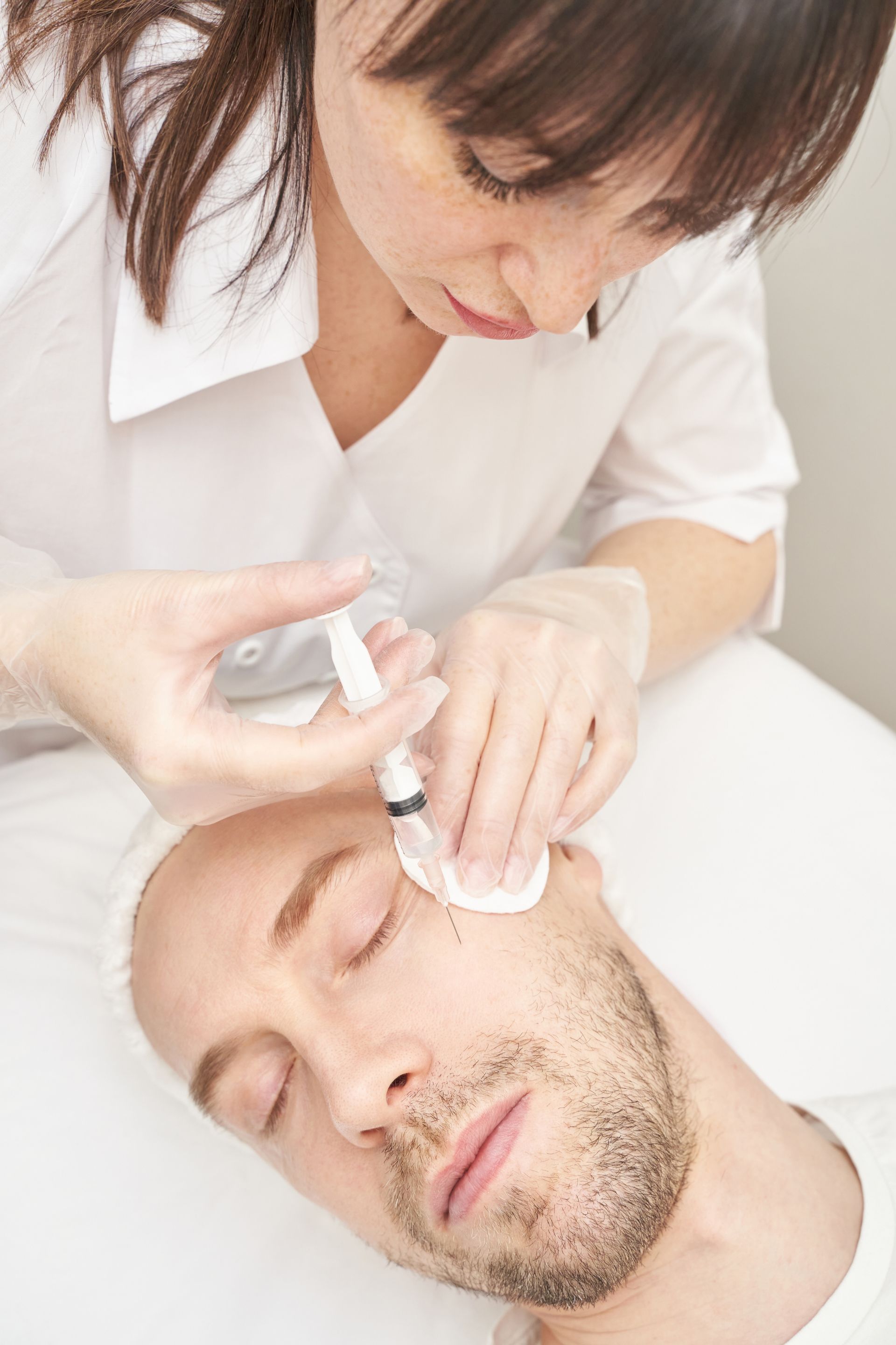 A medical professional injecting a man's face with a syringe in a clinic setting.