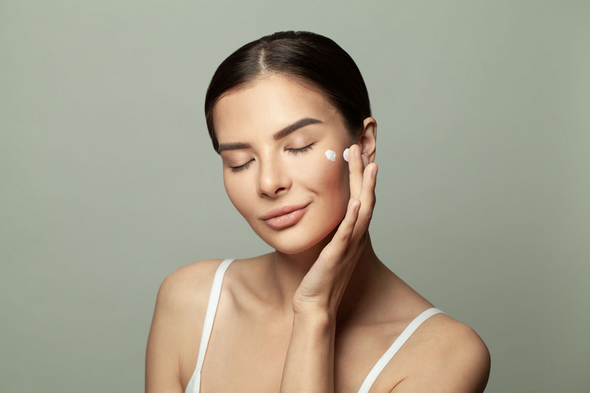 A woman is applying cream to her face.