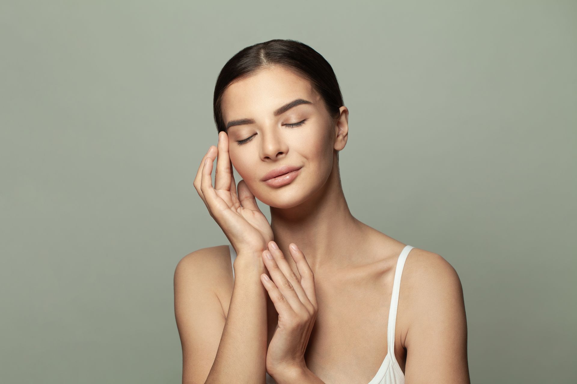 A woman is touching her face with her hands and smiling.