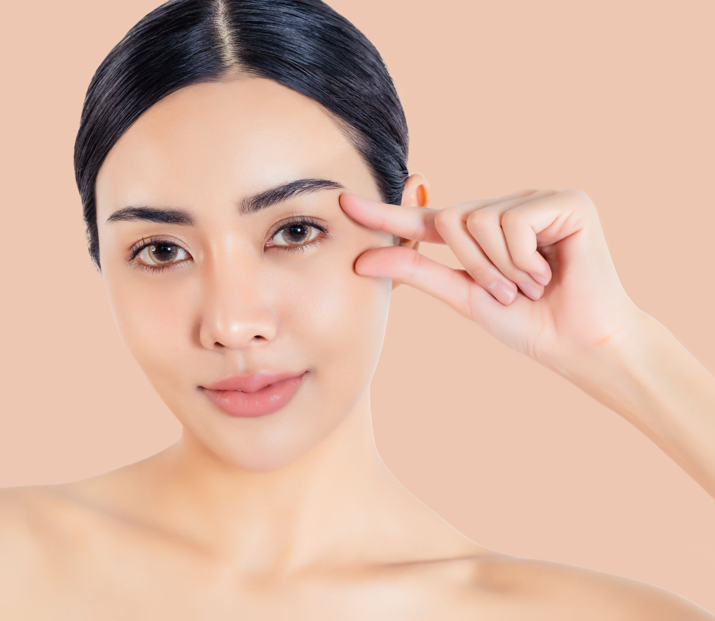 Woman holding fingers near her eye, indicating smallness, on a light orange background.