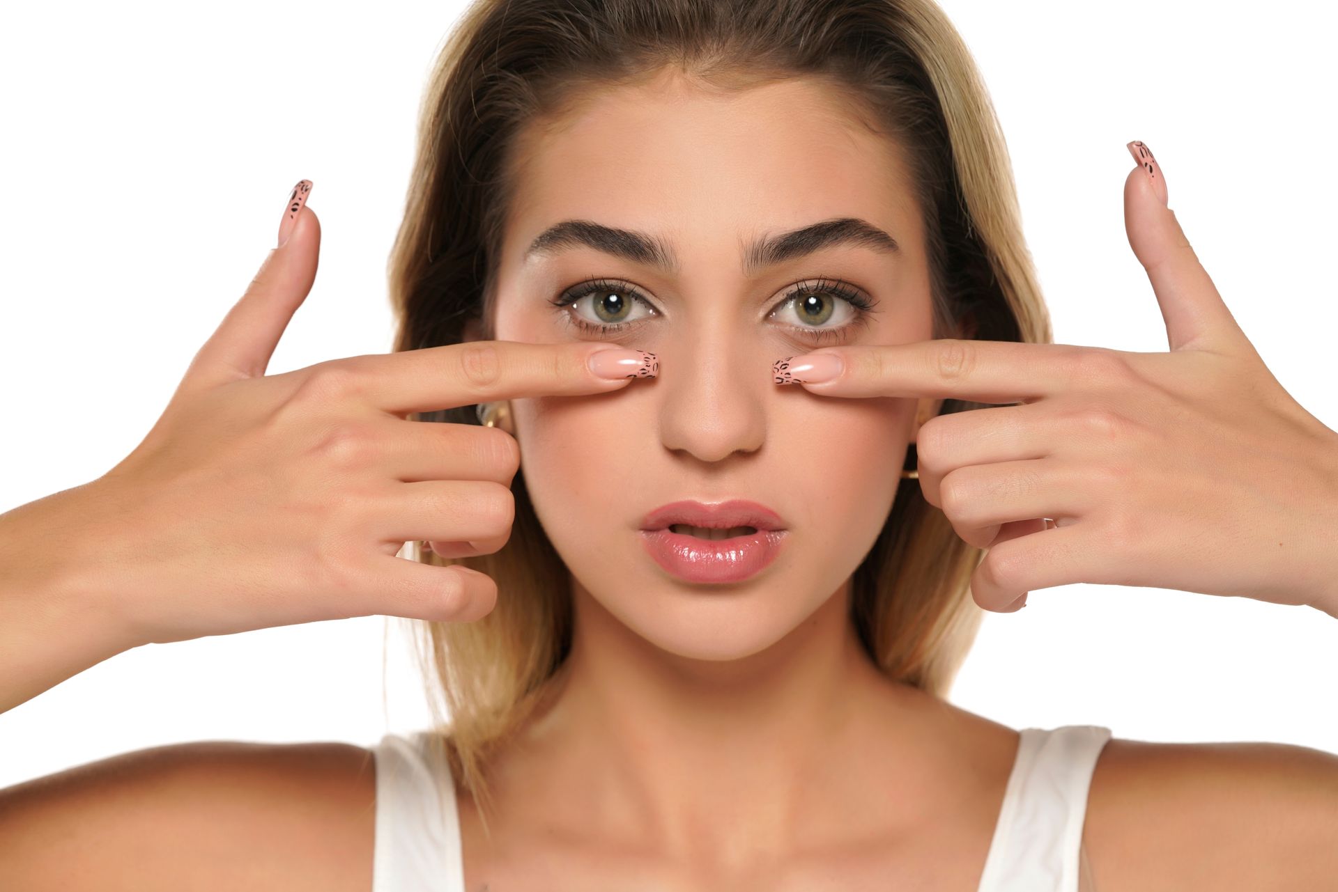 Woman with fingers pointing to her under eyes, looking at the viewer. White background.