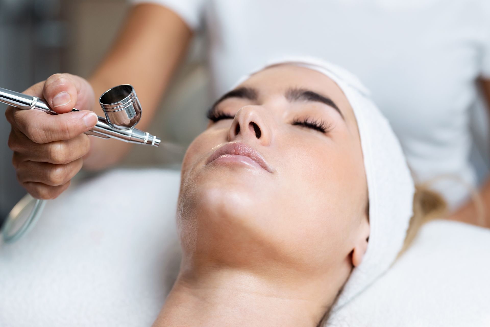 A woman is getting an airbrush treatment on her face.