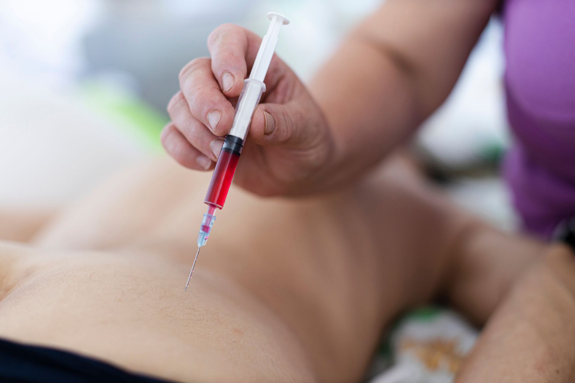 A person is holding a syringe with a red liquid in it.
