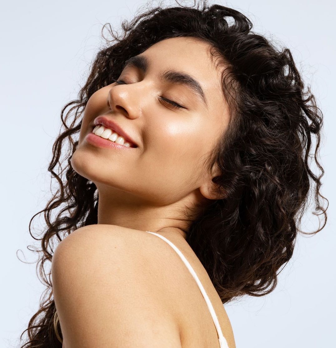 A woman with curly hair is smiling with her eyes closed.