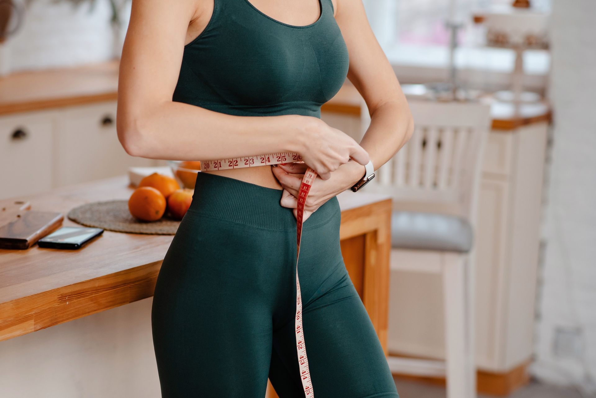 A woman is measuring her waist with a tape measure.