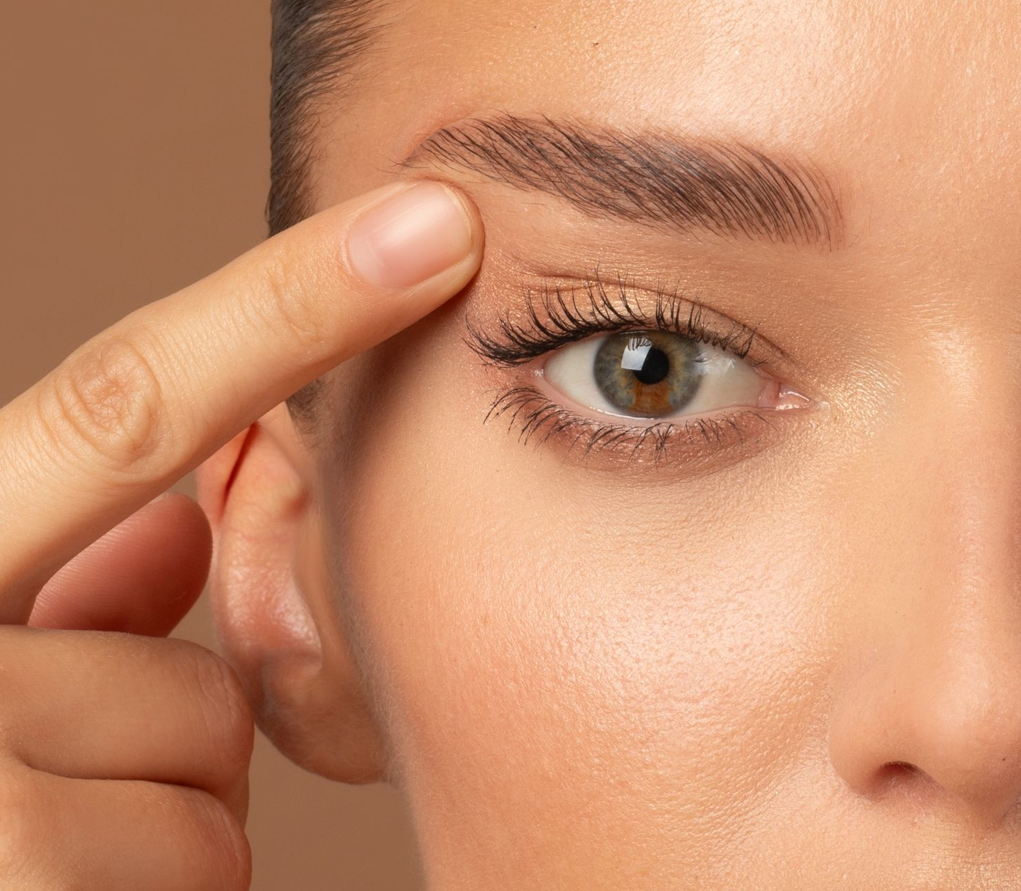 Woman's eye with arched eyebrow. Finger touching brow. Beige background.