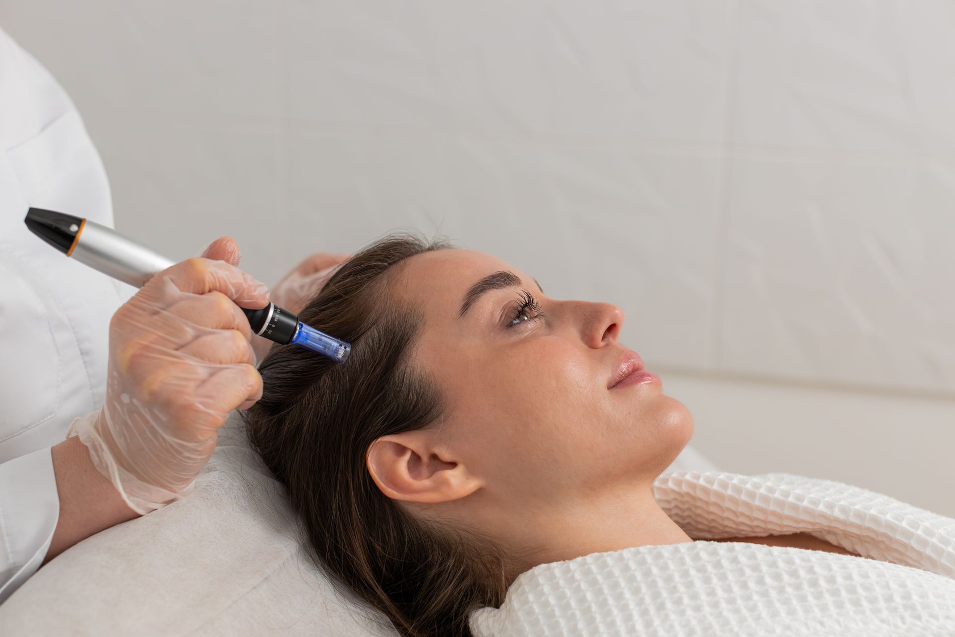 Woman receiving scalp micro-needling treatment at a clinic, lying down with a medical tool.