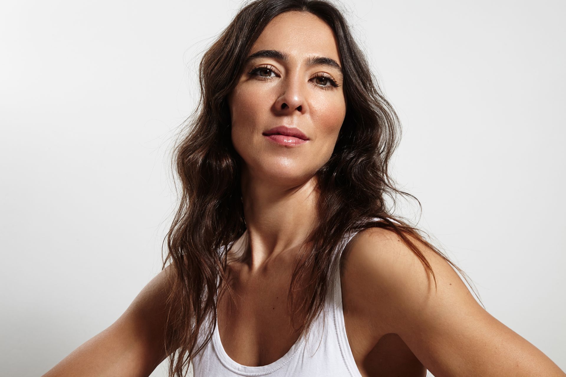 A woman with long hair is wearing a white tank top.