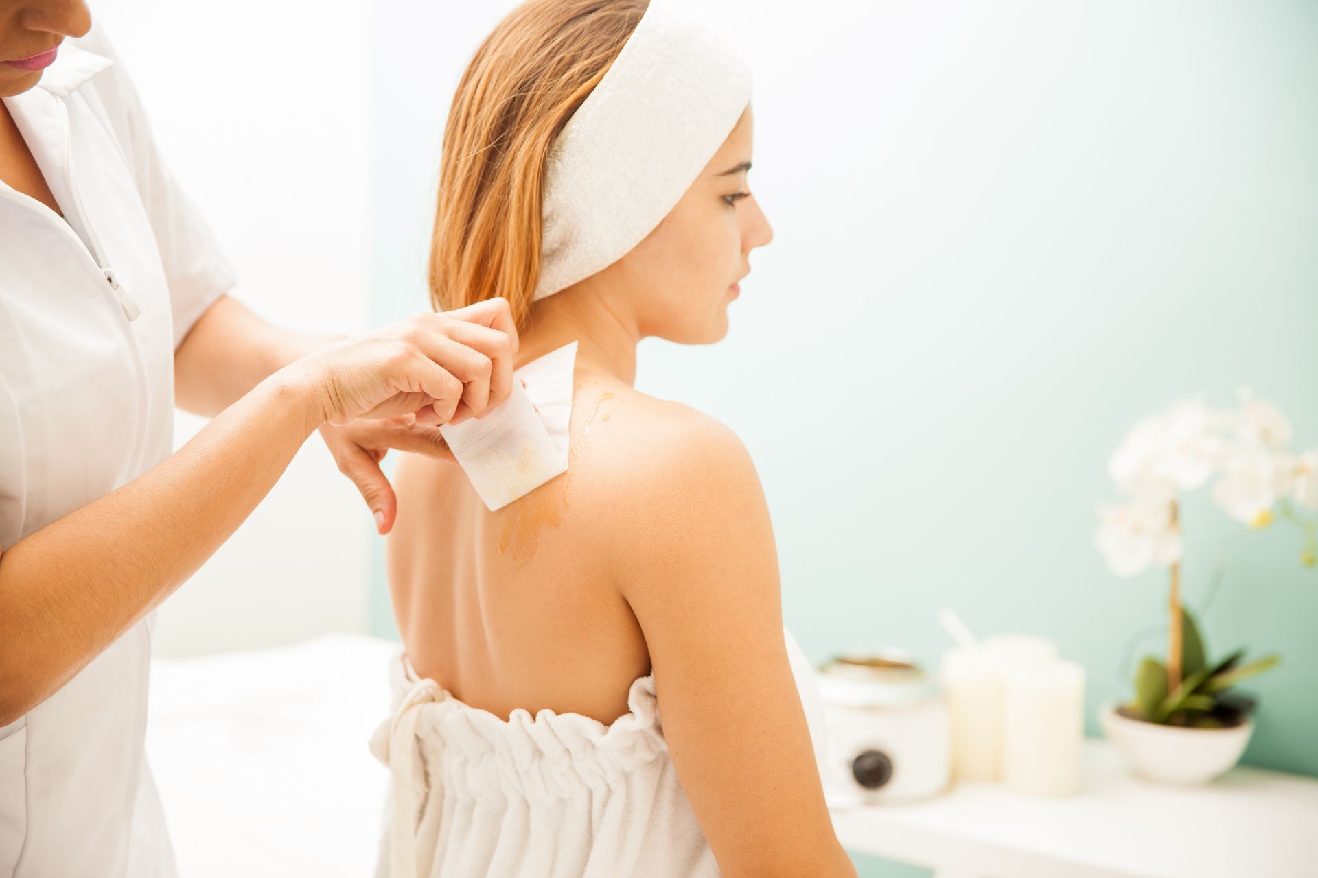 Woman having back waxed at a spa; esthetician holding a wax strip.