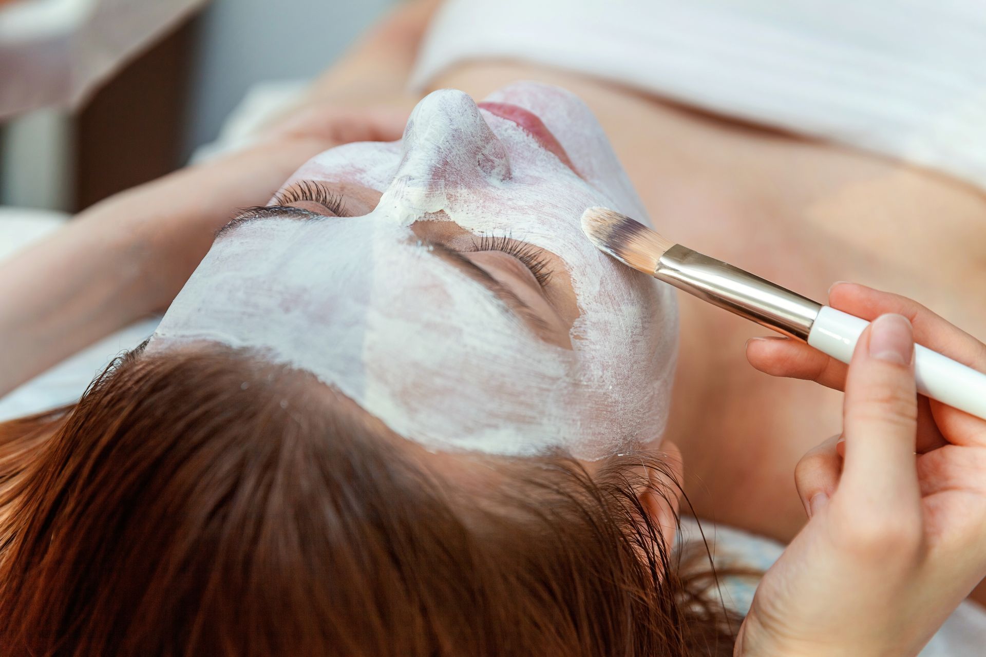 A woman is getting a foam mask on her face.