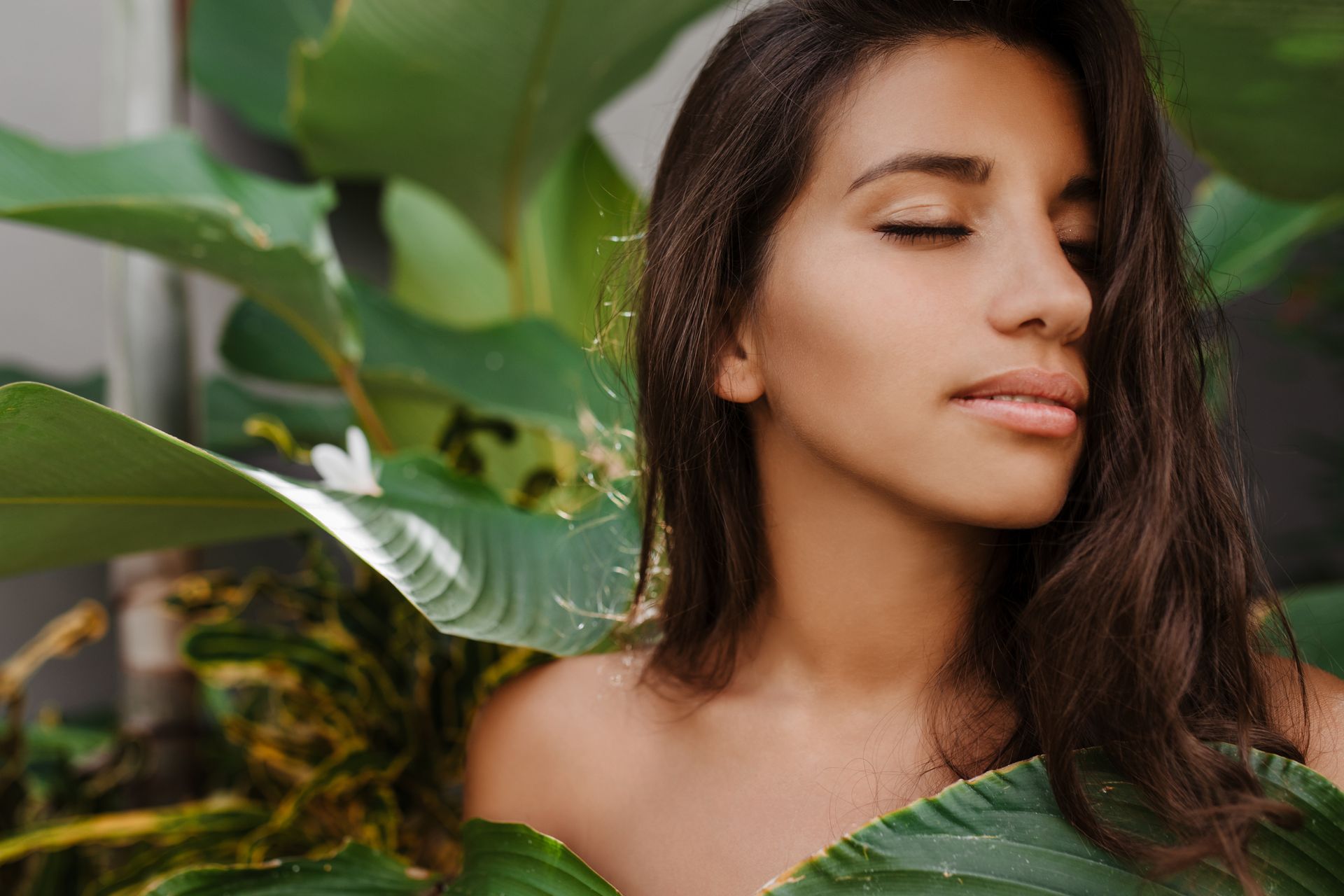 A woman with her eyes closed is surrounded by green leaves.