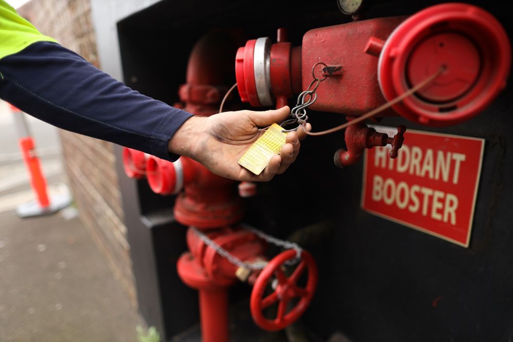Hand Turning a Key on A Red Fire Hydrant Booster Valve Panel — Pasiv Fire in Illawarra, NSW
