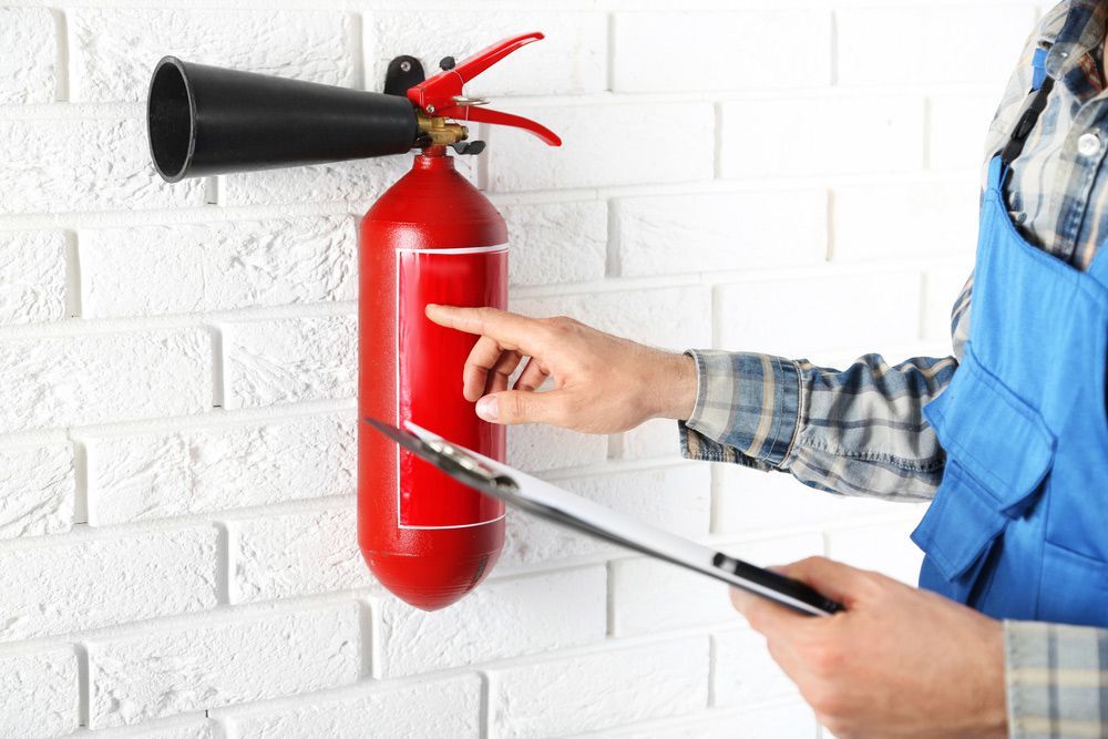 Man Inspecting The Fire Extinguisher Against White Brick — Fire Protection in Cronulla, NSW