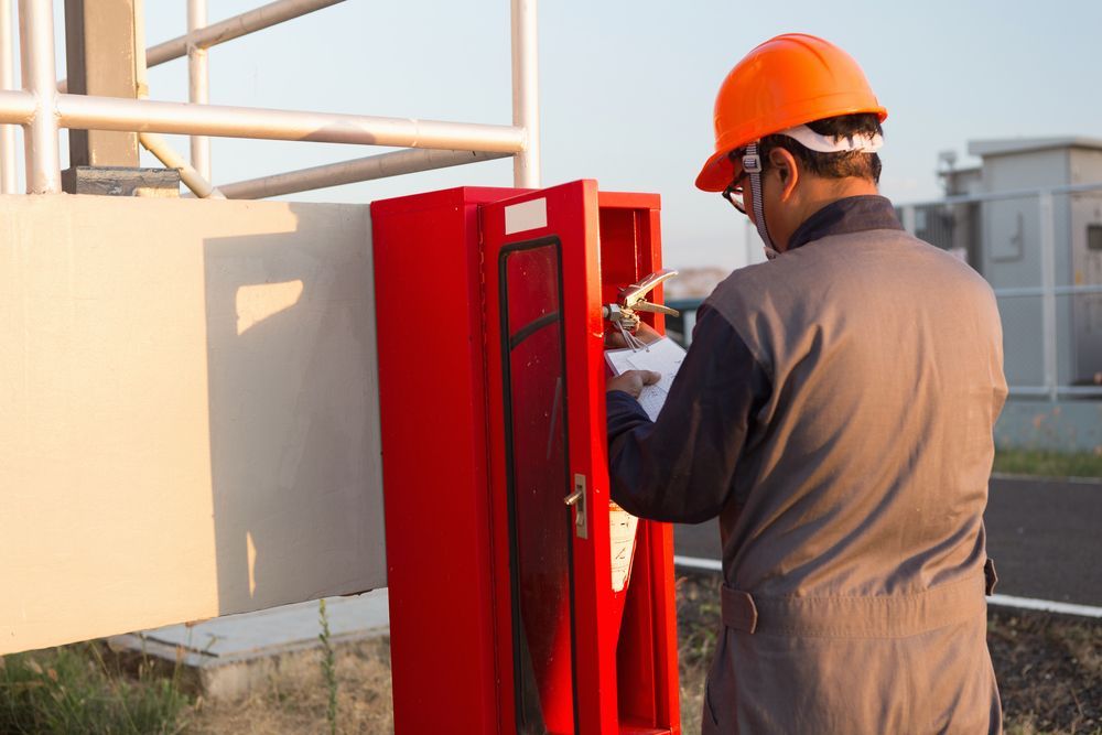 Worker in Orange Hard Hat Inspecting a Red Outdoor Utility Cabinet at A Site — Pasiv Fire in Illawarra, NSW