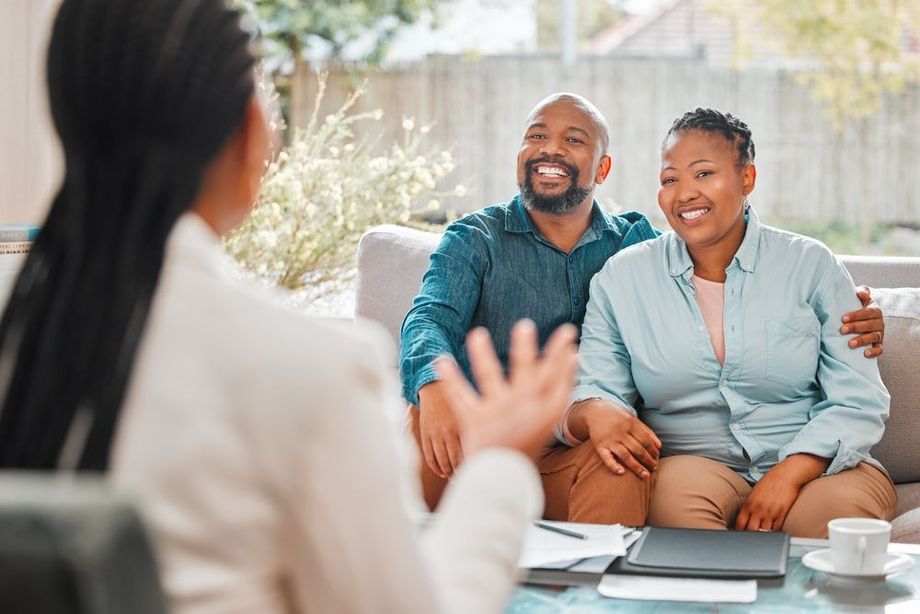 Woman advisor speaking to smiling couple on a couch indoors.