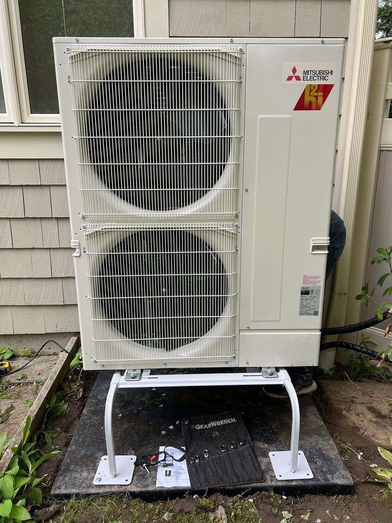 A mitsubishi air conditioner is sitting on top of a concrete platform outside of a house.