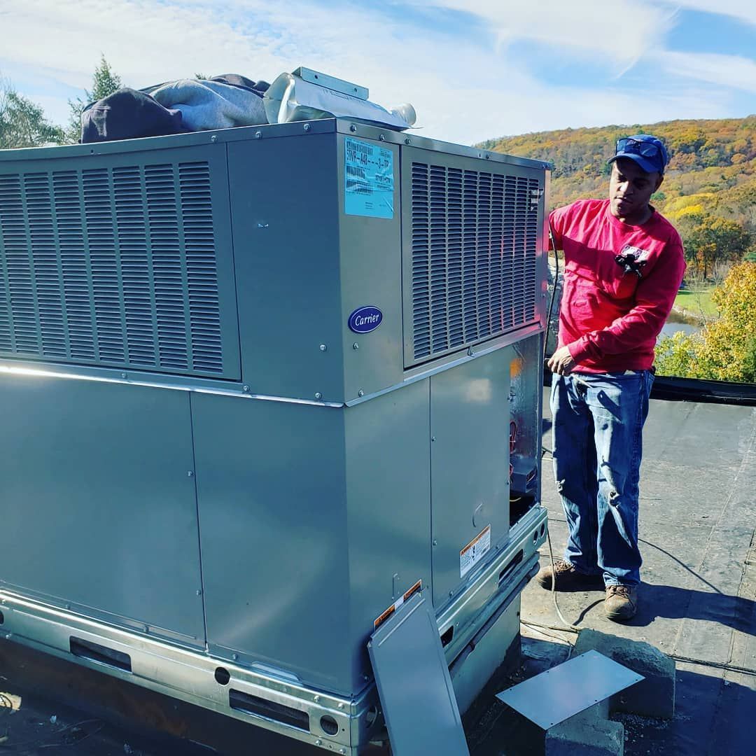 A man is standing next to a large air conditioner on a roof.