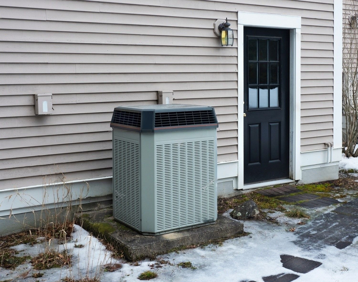 An air conditioner is sitting outside of a house in the snow.