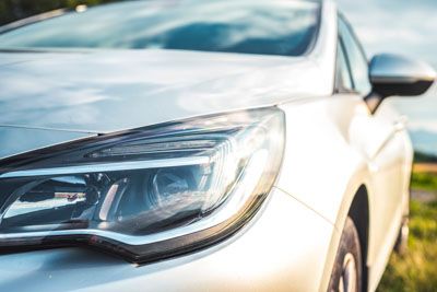 A close up of the headlight of a silver car parked in a field.