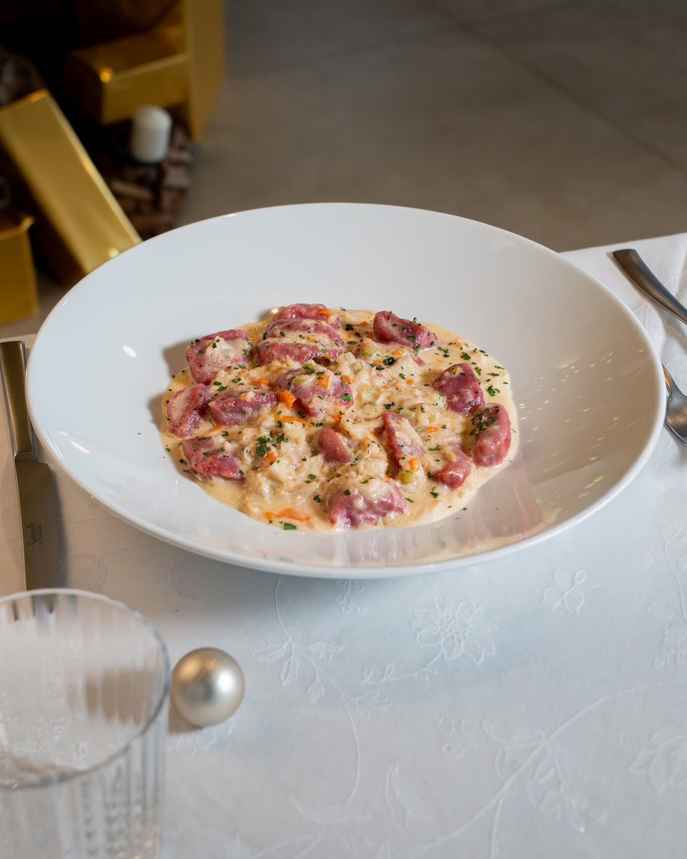 Una ciotola bianca di pasta cremosa con pezzetti di pancetta, adagiata su una tovaglia, con le posate a portata di mano.