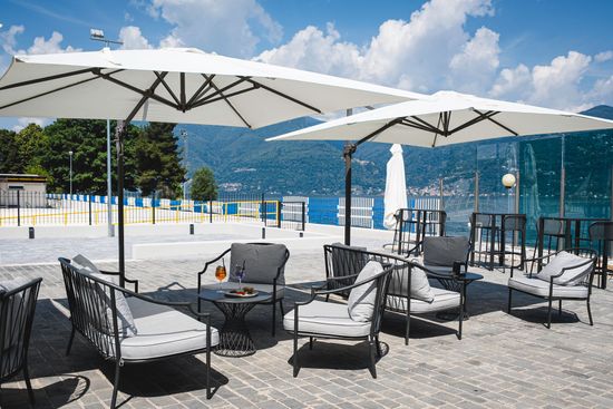 Terrazza sul tetto con ombrelloni bianchi, sedie nere e vista sulla piscina o sul lungomare con le montagne sullo sfondo.