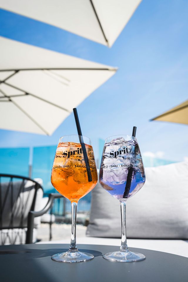 Due cocktail colorati con cannucce su un tavolino da caffè sotto ombrelloni bianchi in riva al mare.