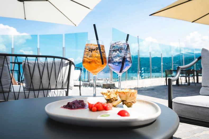 Tavolo da patio esterno con dessert e due bevande ghiacciate con vista su un lungomare soleggiato