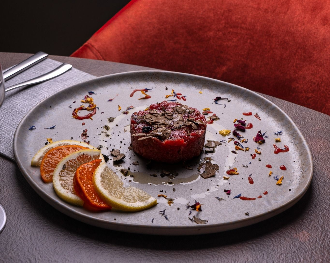 Dessert impiattato con fette di agrumi e guarnizione su un tavolo grigio, con una sedia rossa sullo sfondo.
