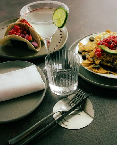 Due tacos con una bevanda su un tavolo, più un piatto e un tovagliolo piegato in un ambiente informale.