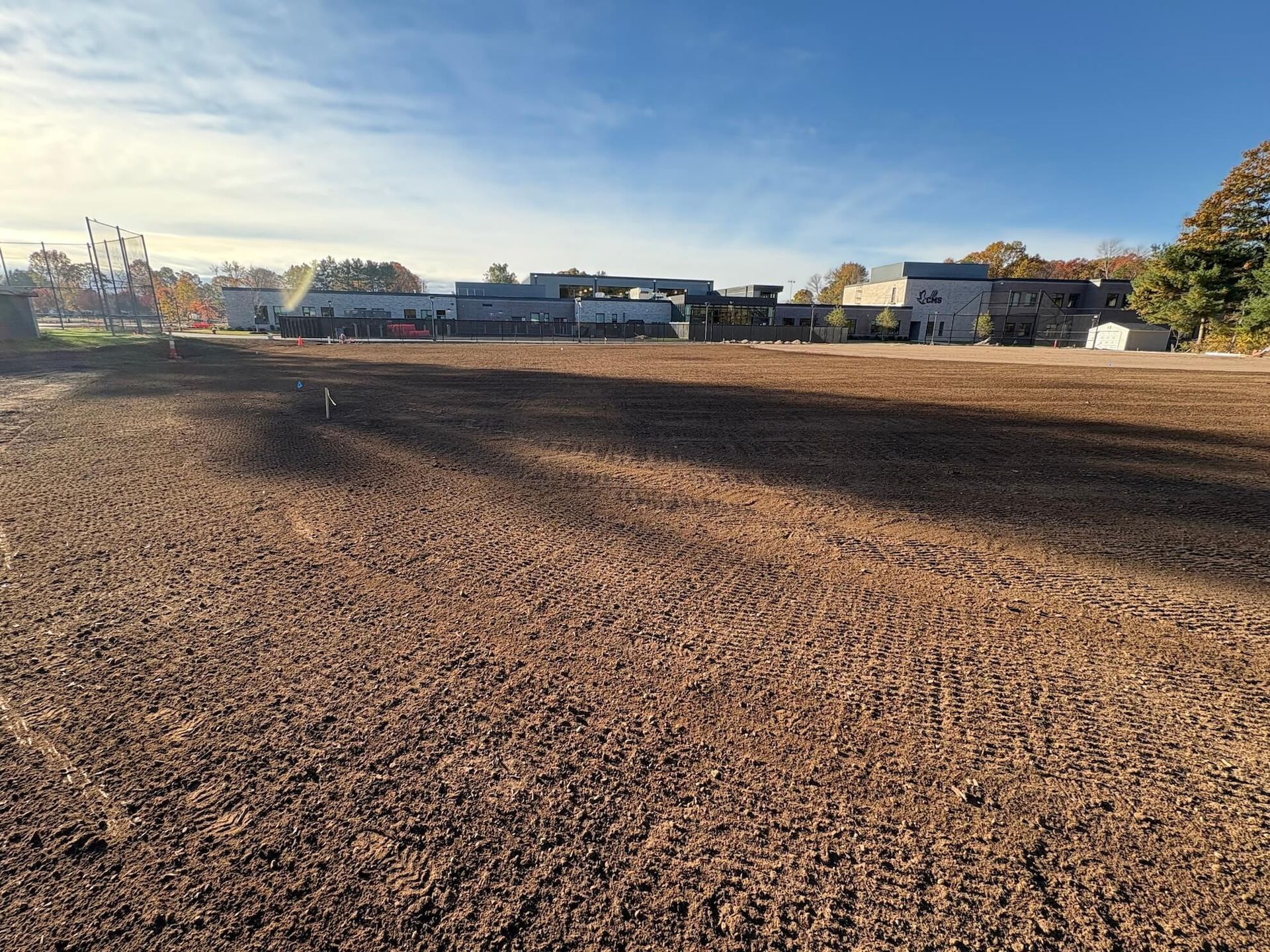 Freshly plowed brown field with houses and trees in the distance under a clear blue sky