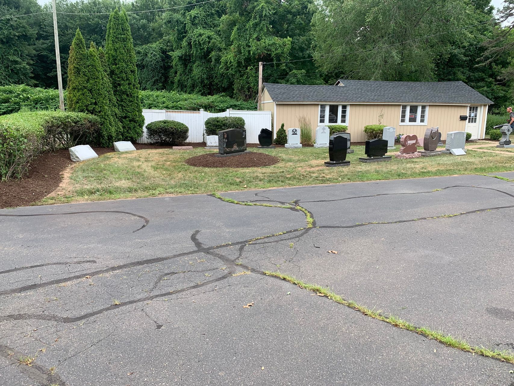 Suburban house with driveway, garage, and landscaped front yard beside a cracked asphalt road.