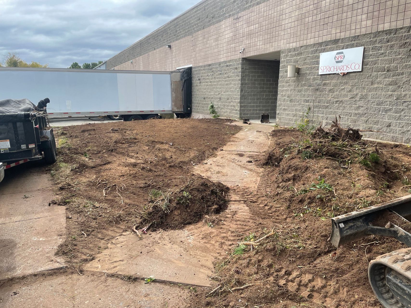 Dirt lot beside a gray brick building with an open gate and scattered debris