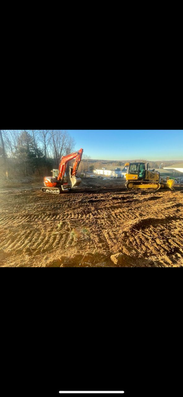 Excavator and bulldozer working on a muddy construction site under a clear blue sky