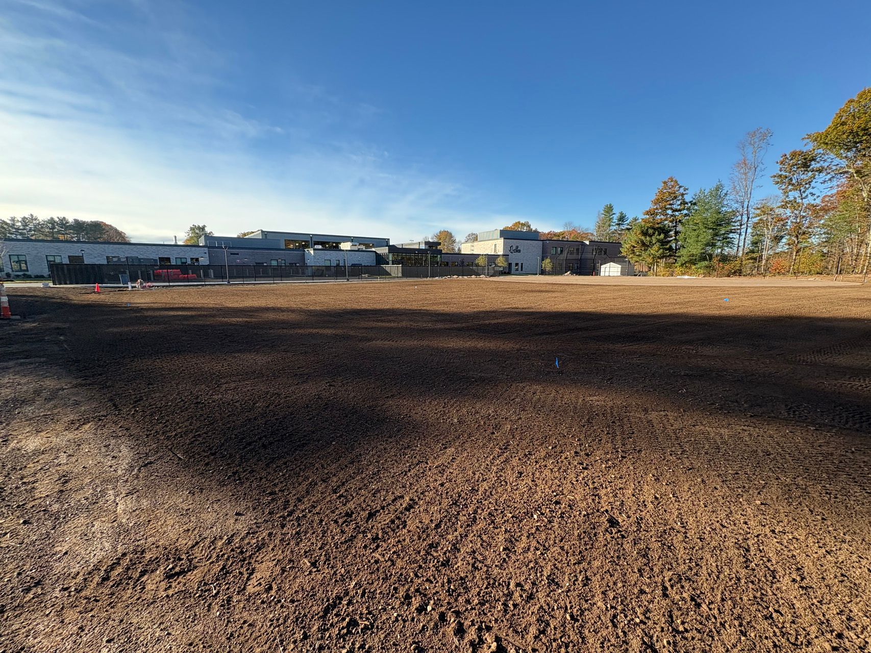 Wide dirt field under a clear blue sky with buildings and trees in the distance