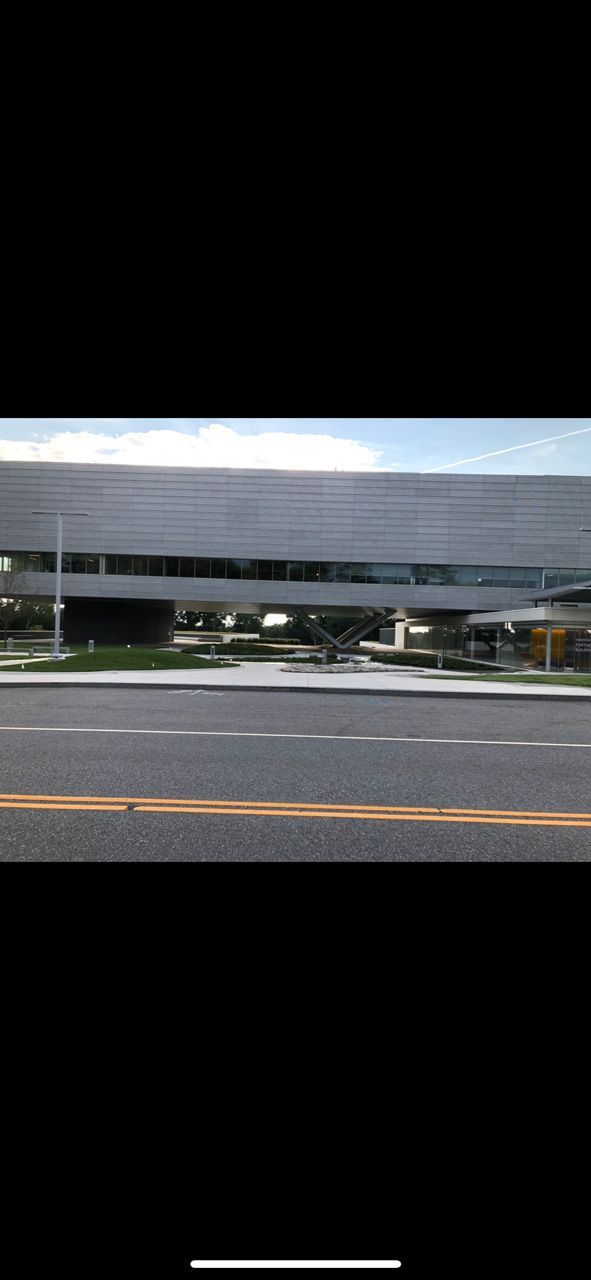 Modern gray building with a curved facade beside a road under a partly cloudy sky