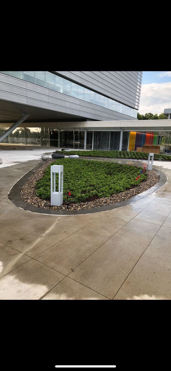 Outdoor building entrance with a landscaped circular planter, concrete walkway, and modern canopy.