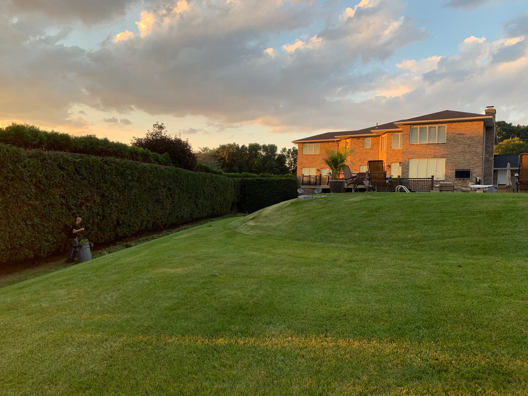 Sunlit stone house beside a large green lawn and tall hedge at sunset