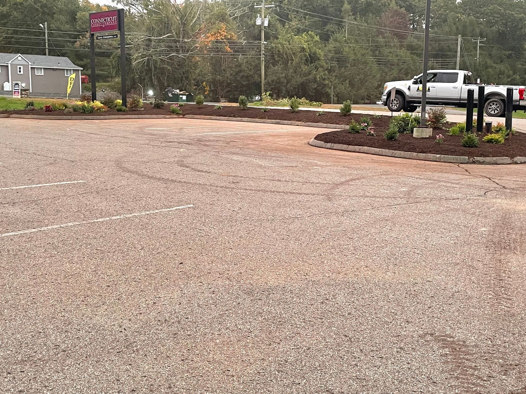 Wet parking lot with a white pickup truck near a landscaped curb and sign on a rainy day