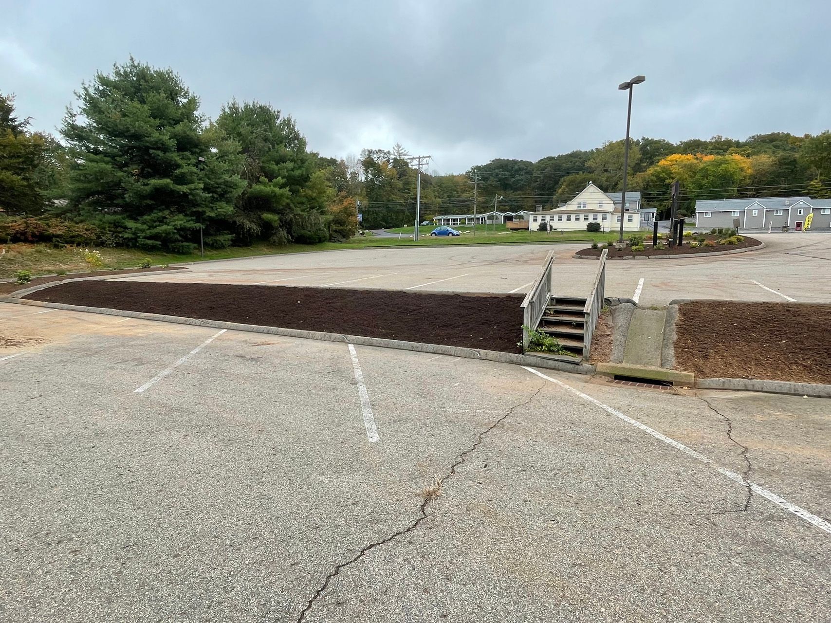 Empty parking lot with a raised mulch bed, steps, trees, and buildings in the background